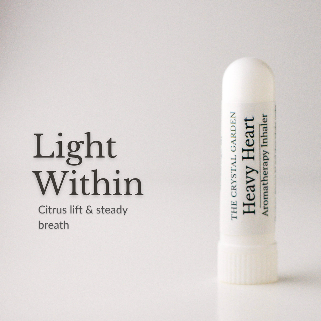 A white cylindrical aromatherapy inhaler tube labeled 'THE CRYSTAL GARDEN Heavy Heart Aromatherapy Inhaler' stands on a light gray background beside the text 'Light Within' and 'Citrus lift & steady breath'.