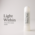 A white cylindrical aromatherapy inhaler tube labeled 'THE CRYSTAL GARDEN Heavy Heart Aromatherapy Inhaler' stands on a light gray background beside the text 'Light Within' and 'Citrus lift & steady breath'.
