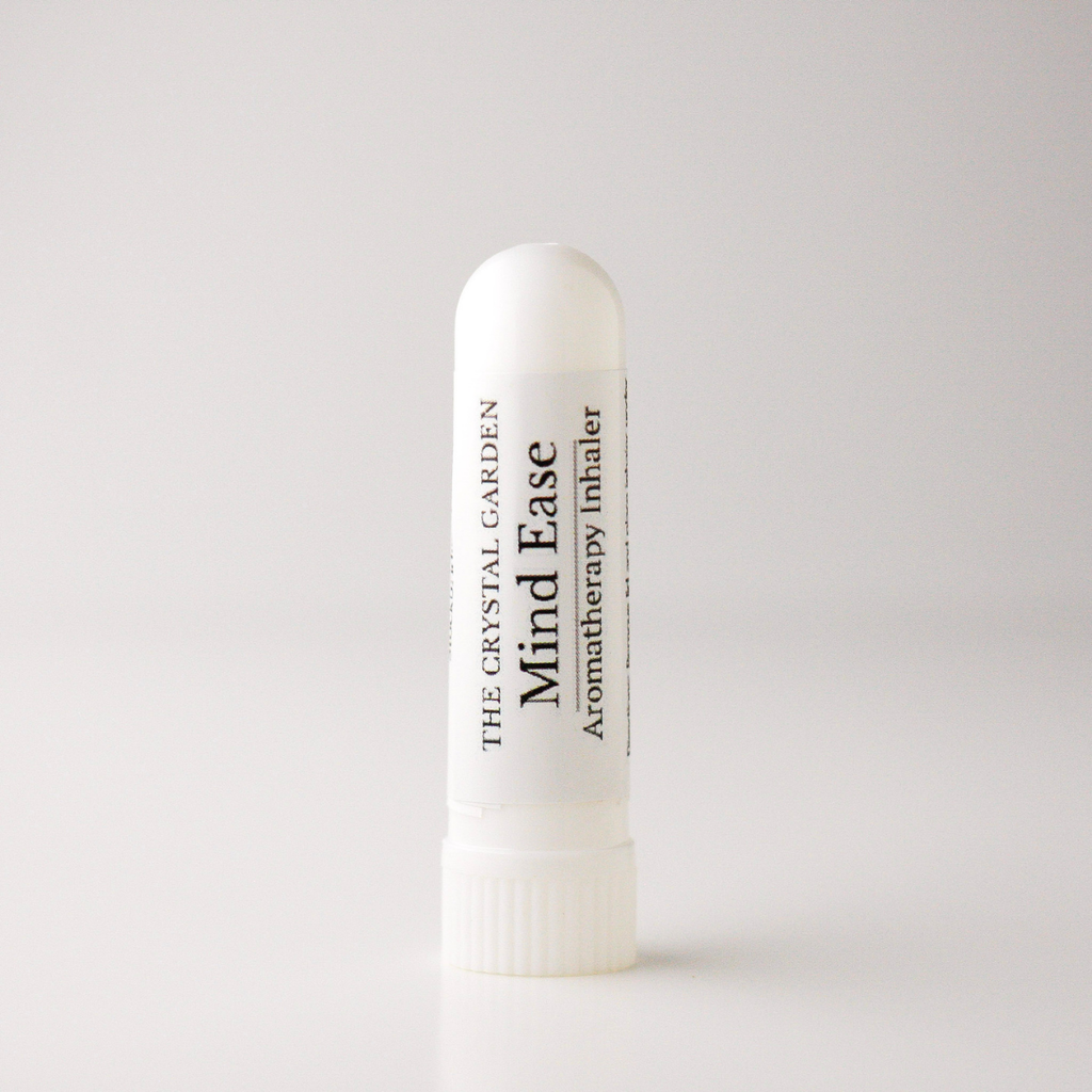 A white cylindrical aromatherapy inhaler tube standing upright on a light gray background. The label reads 'THE CRYSTAL GARDEN Mind Ease Aromatherapy Inhaler' in black text.