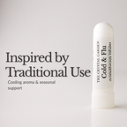 A white cylindrical aromatherapy inhaler tube stands on a light gray background next to black text that reads 'Inspired by Traditional Use' and 'Cooling aroma & seasonal support.' The tube is labeled 'THE CRYSTAL GARDEN Cold & Flu Aromatherapy Inhaler.