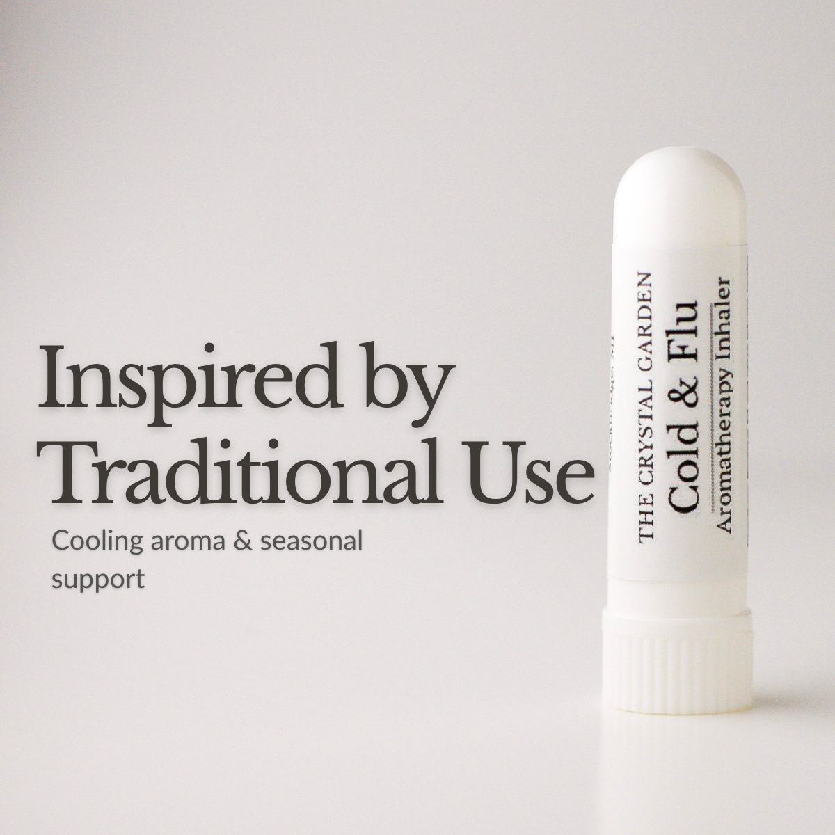 A white cylindrical aromatherapy inhaler tube stands on a light gray background next to black text that reads 'Inspired by Traditional Use' and 'Cooling aroma & seasonal support.' The tube is labeled 'THE CRYSTAL GARDEN Cold & Flu Aromatherapy Inhaler.