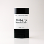 A single stick of salve from The Crystal Garden, Cold & Flu Botanical Salve, in a black and white container, centered on a light gray background.