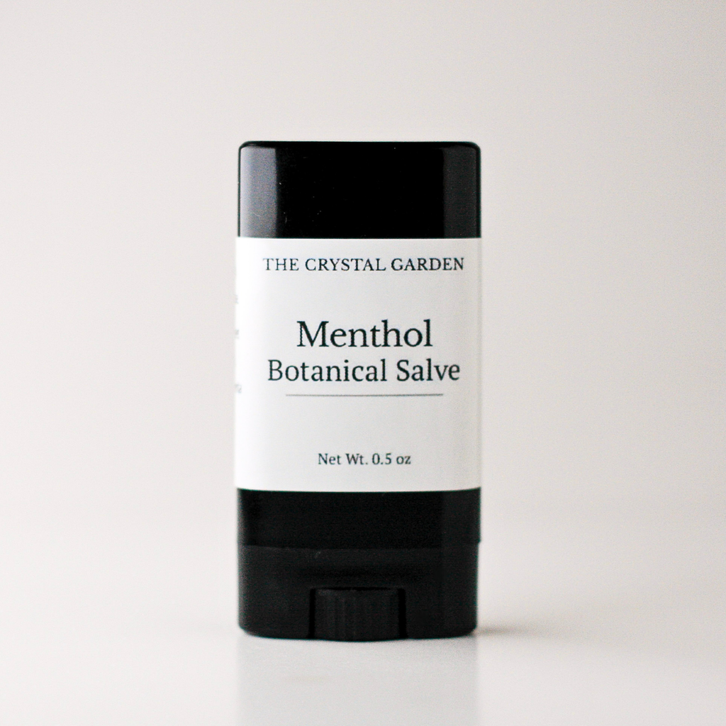 A single stick of The Crystal Garden Menthol Botanical Salve, featuring a black container with a white label, centered on a light gray background.