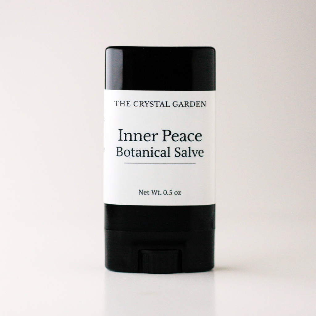 A single stick of salve from The Crystal Garden, specifically Inner Peace Botanical Salve, in a black plastic container with a white paper label, set against a plain light background.